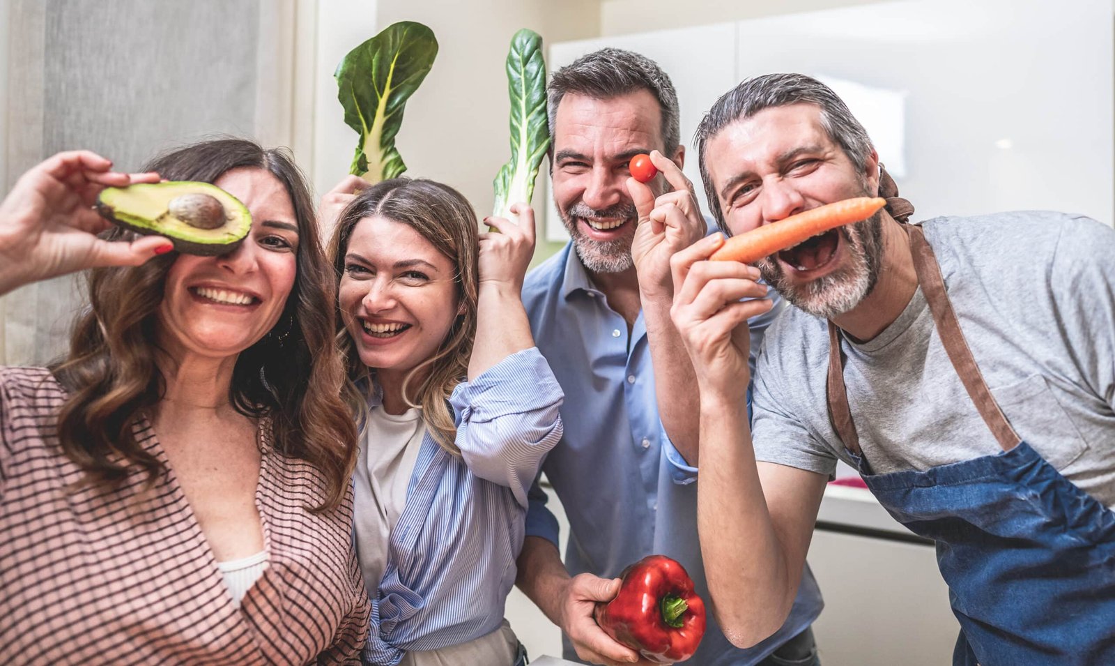 Four adult friends cooking together and taking photos with bio food in the kitchen