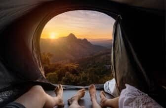 Young couple lying in camping tent and looking at sunset over the mountain