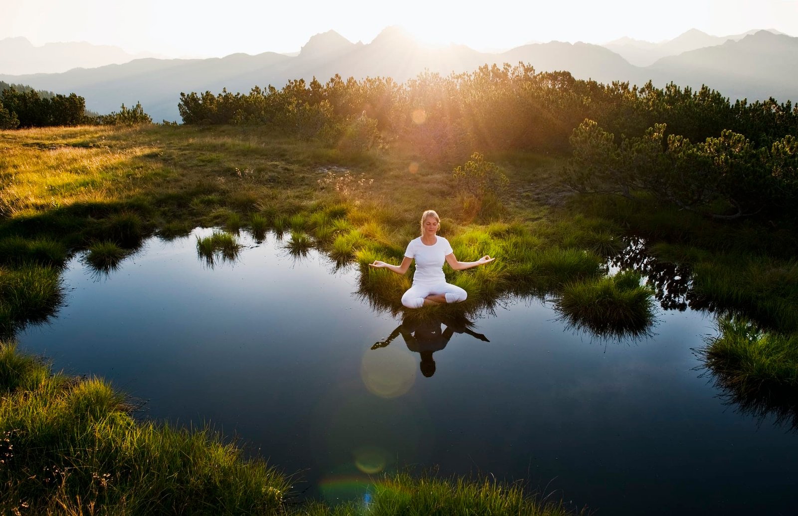 Austria, Salzburg County, Young woman sitting near mountain lake and doing meditation
