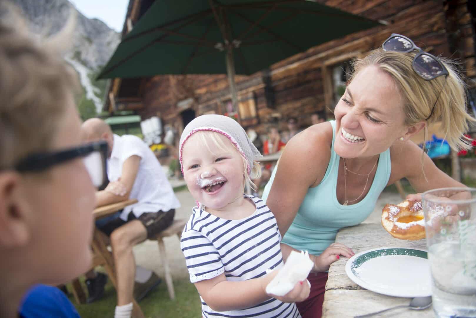 Happy little girl eating cake with family at alpine hut