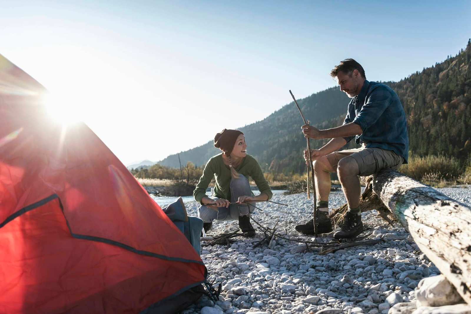 Mature couple camping at riverside, with wood for a camp fire