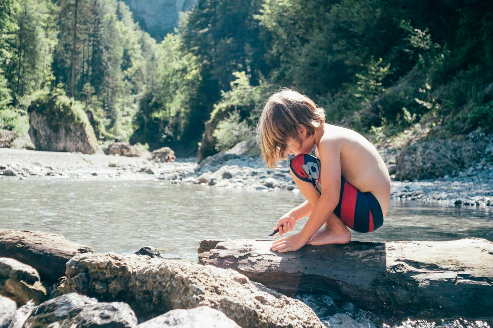 Side view of boy crouching by river playing with pebbles, Bludenz, Vorarlberg, Austria