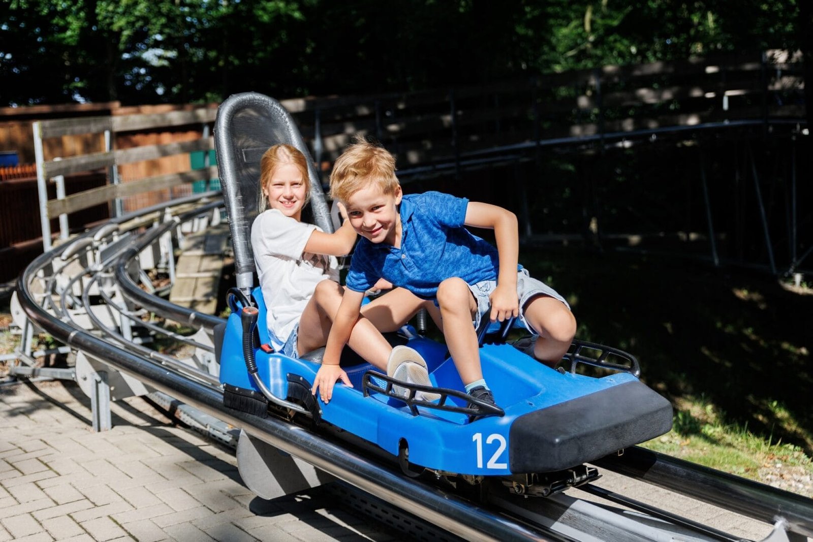 Pair of cute laughing kids enjoy have fun riding alpine roller coaster cart together at Harz