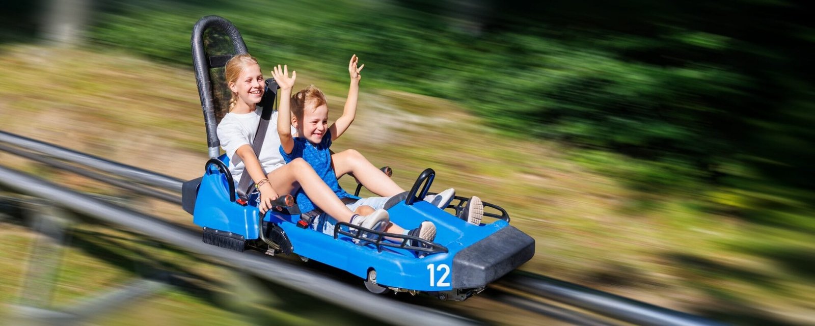 Pair of cute laughing kids enjoy have fun riding alpine roller coaster cart together